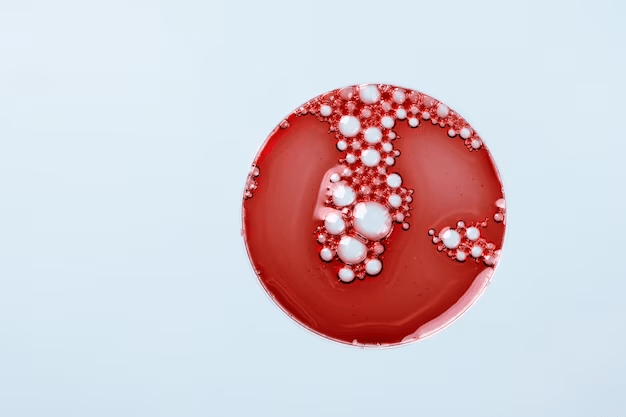 A red petri dish with white circular colonies of bacteria or fungi on its surface, set against a plain light blue background.