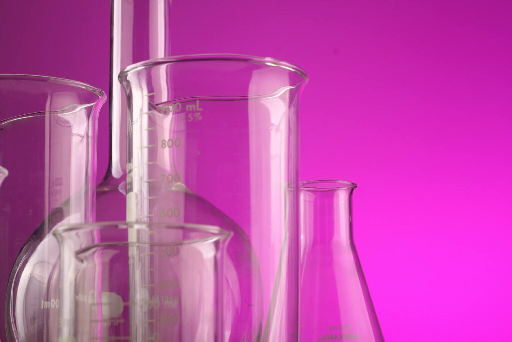Several empty glass laboratory beakers and flasks are grouped together against a pink background.