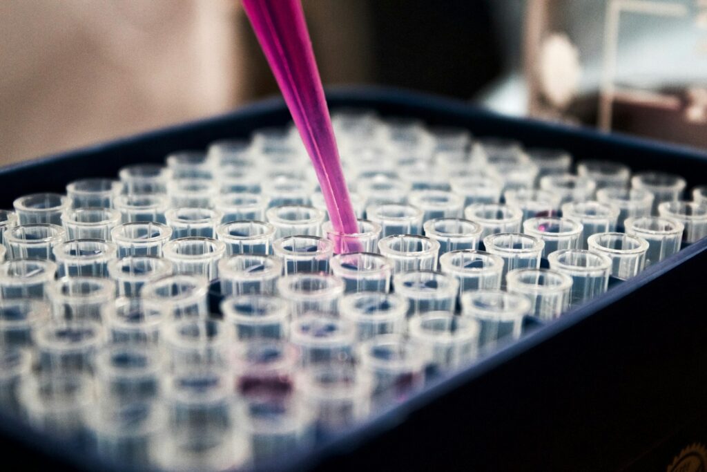 A purple liquid is being dispensed with a pipette into clear plastic tubes arranged in a tray, commonly used in laboratory settings.